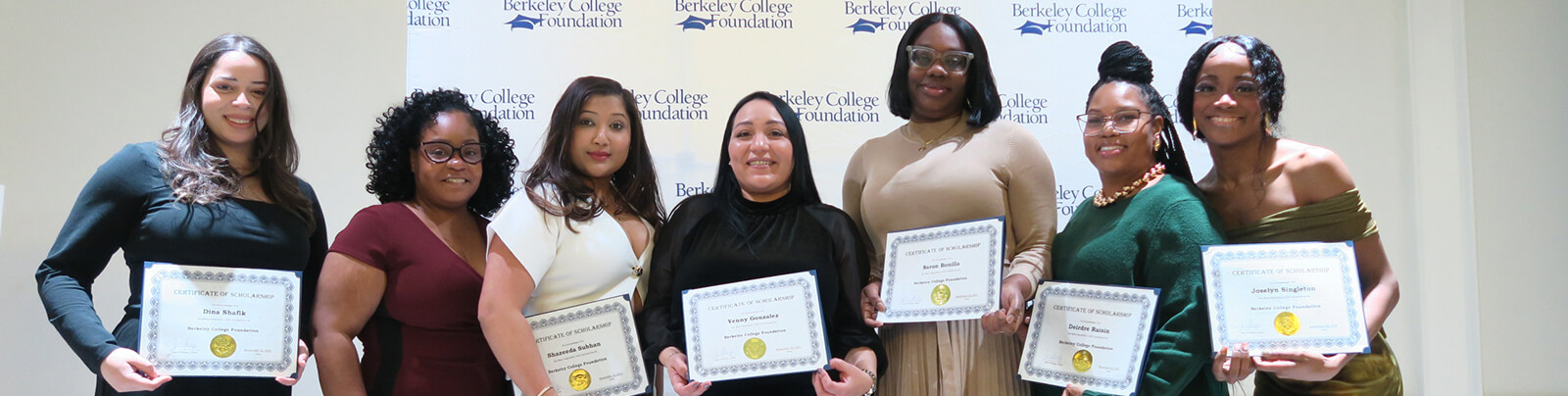People with certificates stand in a line smiling and posing for the camera