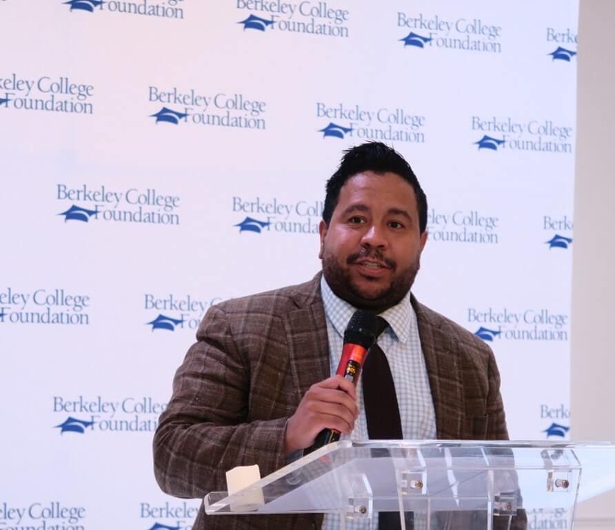 A man with a microphone stands at a podium giving a speech