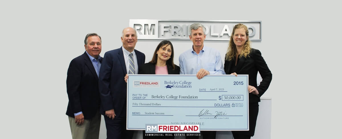 Group photo in an office setting, featuring five individuals holding a large ceremonial check to the Berkeley College Foundation