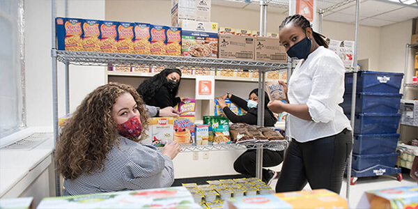 Two women wearing protective gear supporting each other in a pantry setting