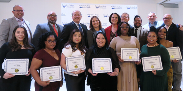 A group of individuals posing with certificates in front of a branded backdrop, celebrating achievements at a recognition event.